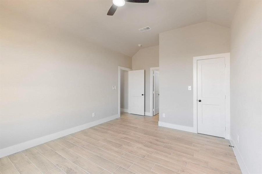 Unfurnished bedroom with visible vents, light wood finished floors, baseboards, ceiling fan, and vaulted ceiling