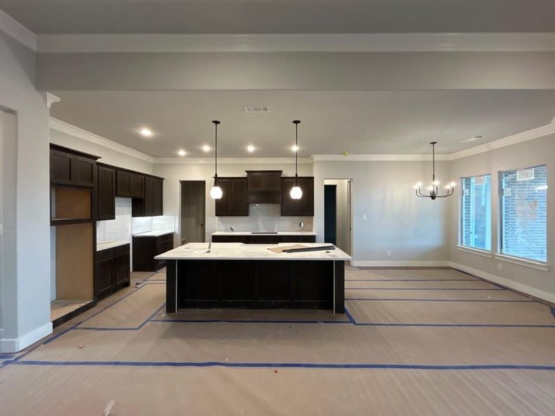 Kitchen featuring crown molding, hanging light fixtures, a center island, dark brown cabinetry, and decorative backsplash