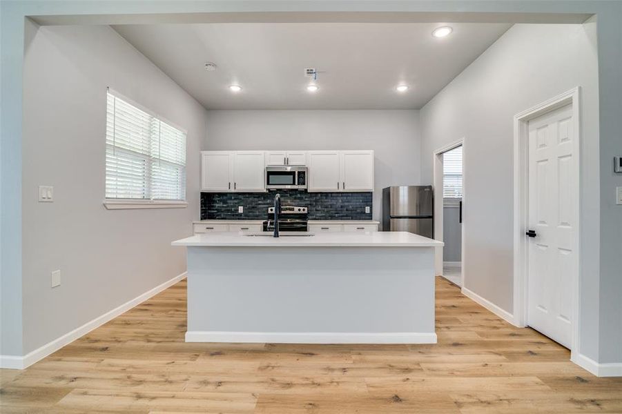Kitchen with stainless steel appliances, plenty of natural light, white cabinets, and decorative backsplash