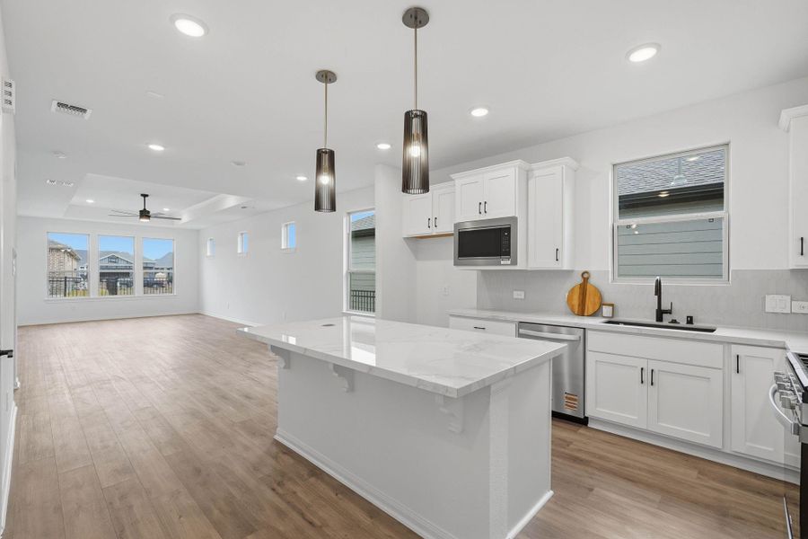 Open-concept modern kitchen with a large island, white cabinetry and stainless steel appliances, flowing into a bright living area with recessed lighting and abundant natural light.