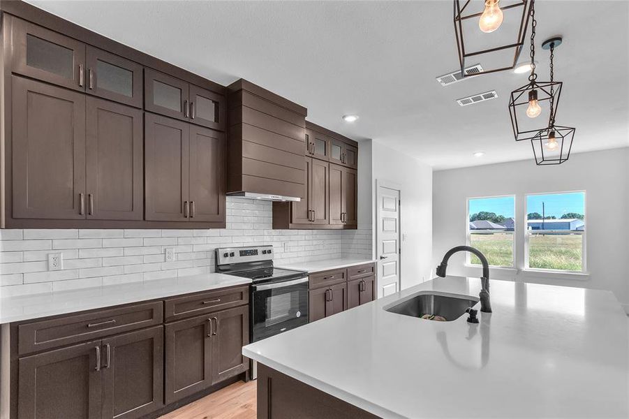 Kitchen featuring light hardwood / wood-style floors, tasteful backsplash, sink, hanging light fixtures, and electric stove Kitchen featuring light hardwood / wood-style floors, tasteful backsplash, sink, hanging light fixtures, and electric stove