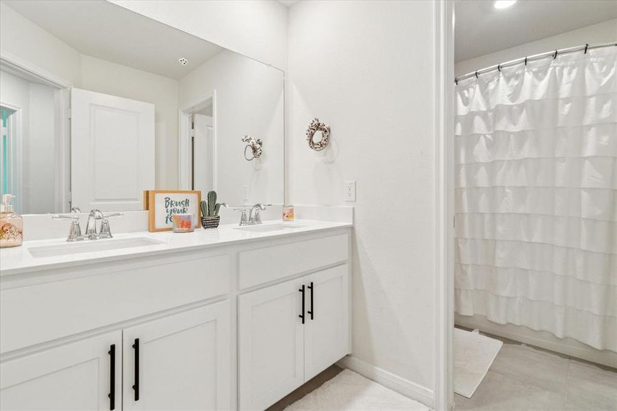 Bathroom featuring double vanity, light tile patterned floors, and shower / bathtub combination with curtain Bathroom featuring double vanity, light tile patterned floors, and shower / bathtub combination with curtain