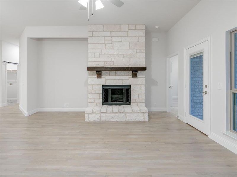 Unfurnished living room with light hardwood / wood-style floors, a stone fireplace, and ceiling fan