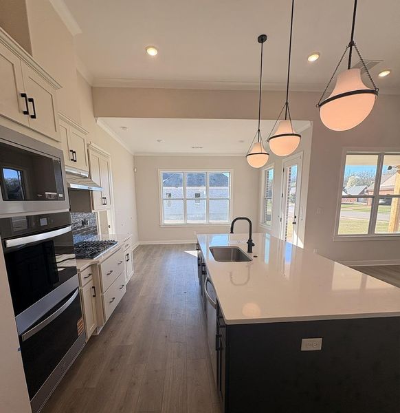 Kitchen featuring two tone cabinets, stainless steel appliances, a kitchen island with sink, dark wood-style flooring, and pendant lighting