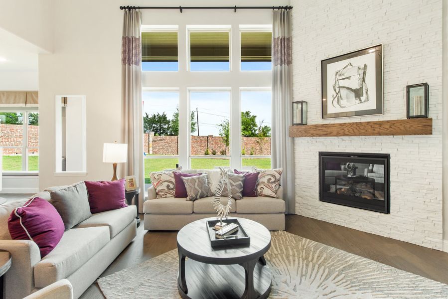 Living room with white brick fireplace, tall windows, and two gray sofas with purple accent pillows Living room with white brick fireplace, tall windows, and two gray sofas with purple accent pillows