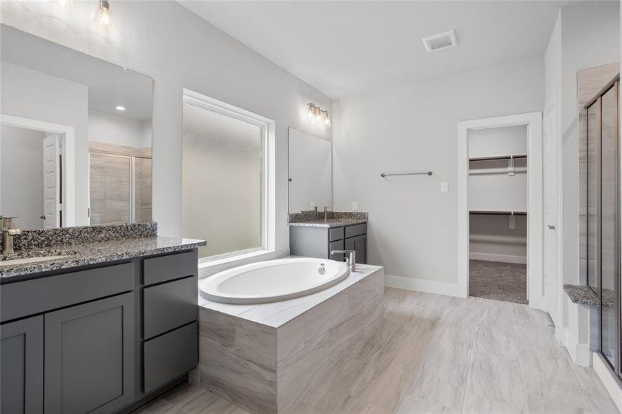 This primary bathroom is definitely move-in ready! Featuring a framed walk-in shower with tile surround, separate garden tub for soaking after a long day with custom tile detailing, grey cabinets with light countertops, spacious walk-in closet with shelving, high ceilings, custom paint, sleek and modern finishes.