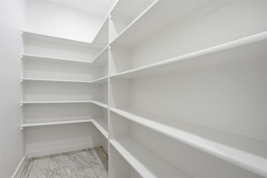 Corner pantry featuring extensive white shelving, white walls, white baseboards, and grey patterned tile flooring