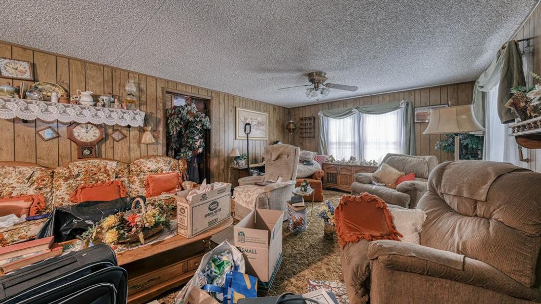 Living room with a textured ceiling, ceiling fan, and wooden walls