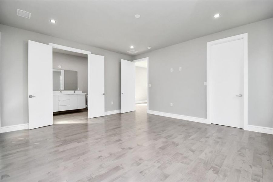 This is a spacious, well-lit room with modern grey flooring, neutral wall colors, recessed lighting, and two doors leading to other rooms, suggesting an en-suite bathroom.