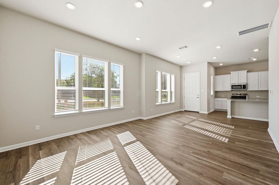 Open-concept living area with wood-finish flooring, recessed lighting, and multiple windows with blinds Open-concept living area with wood-finish flooring, recessed lighting, and multiple windows with blinds