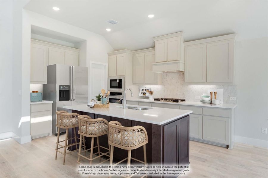Kitchen with white cabinets, dark island with seating, stainless appliances, and light wood floors