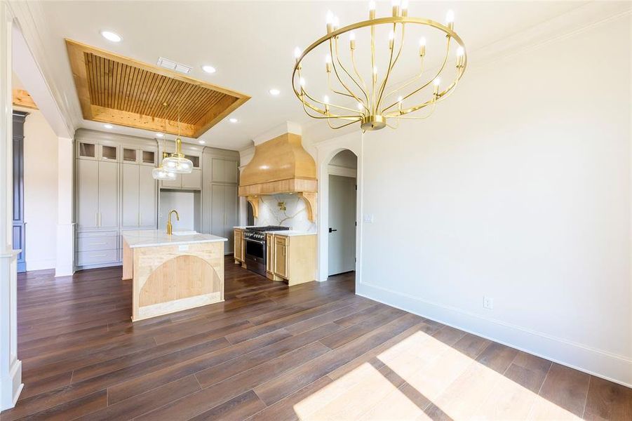 Kitchen featuring dark wood-style flooring, a center island with sink, high end range, tasteful backsplash, and light wood finish cabinetry