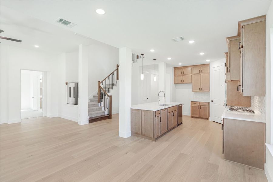 Open-concept kitchen with wood cabinets, center island, and light hardwood floors, open to living area with staircase. Open-concept kitchen with wood cabinets, center island, and light hardwood floors, open to living area with staircase.