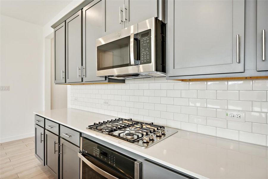 Kitchen featuring backsplash, gray cabinetry, stainless steel appliances, and light wood-type flooring