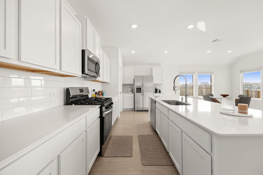 An open concept kitchen features sleek white cabinetry, stainless steel appliances, and ample counter space for culinary endeavors.