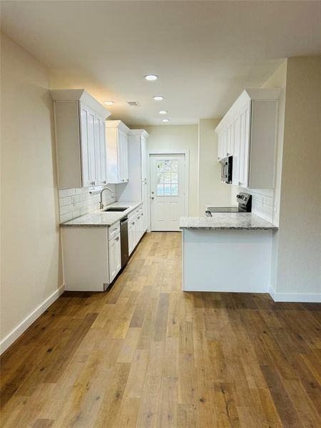 Kitchen with white cabinets, sink, light hardwood / wood-style flooring, appliances with stainless steel finishes, and light stone counters