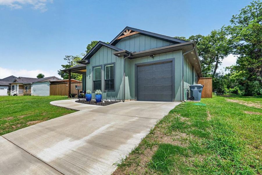 Contemporary residence featuring board and batten siding with a charcoal trim, an attached garage, a concrete driveway, a covered front porch, and mature trees