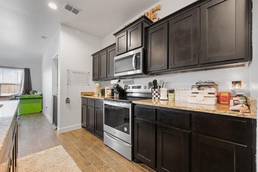 Kitchen with stainless steel appliances, wood finish floors, light stone countertops, and lofted ceiling Kitchen with stainless steel appliances, wood finish floors, light stone countertops, and lofted ceiling