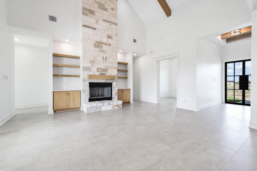Spacious living area with high ceilings, a stone fireplace, built-in shelving, and plenty of natural light.