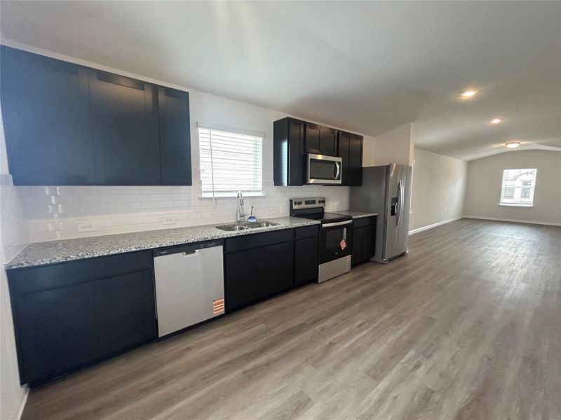 Kitchen featuring stainless steel appliances, lofted ceiling, backsplash, light stone countertops, and light wood-type flooring