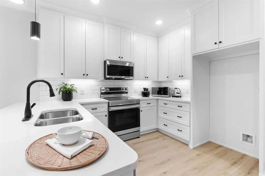 Kitchen with stainless steel appliances, light wood finished floors, decorative backsplash, white cabinets, and recessed lighting