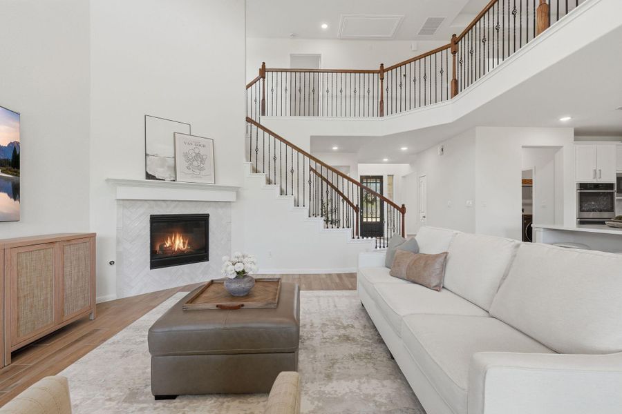 This spacious living room features high ceilings, a cozy fireplace, and a stylish staircase with wrought iron railings. The open floor plan connects to a modern kitchen, creating an inviting atmosphere for entertaining.