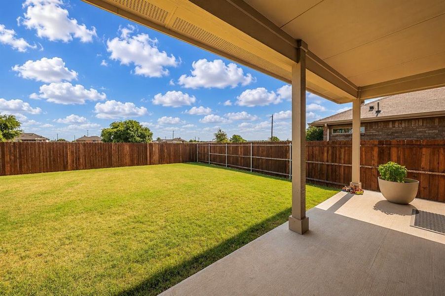 Expansive backyard featuring a large grass lawn, privacy fencing, and a concrete patio with a covered overhang