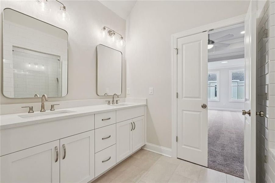 Bathroom featuring light carpet, double vanity, tiled shower, light tile patterned floors, and a ceiling fan