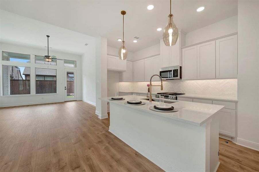 Open-concept kitchen and living area featuring wood-finish flooring, white cabinetry, a kitchen island with seating, a herringbone tile backsplash, and stainless steel appliances