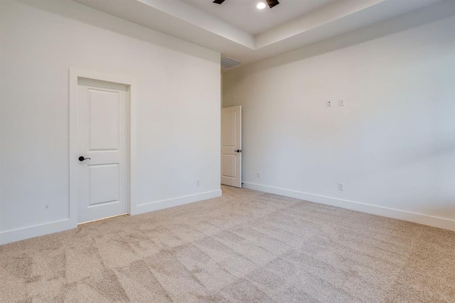 Empty room with light carpet, a ceiling fan, and a raised ceiling