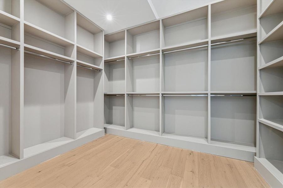 This primary closet features custom built-in shelving, hanging rods, and light wood flooring, offering a spacious and organized storage solution.