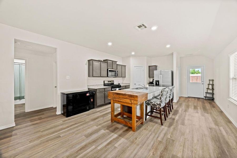 Open concept living space featuring wood-finish flooring, recessed lighting, and a kitchen with gray cabinetry Open concept living space featuring wood-finish flooring, recessed lighting, and a kitchen with gray cabinetry