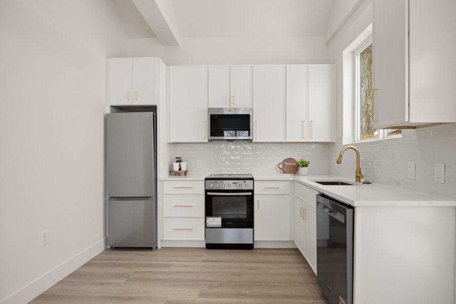 Kitchen featuring stainless steel appliances, white cabinets, tasteful backsplash, light wood-style flooring, and light stone counters