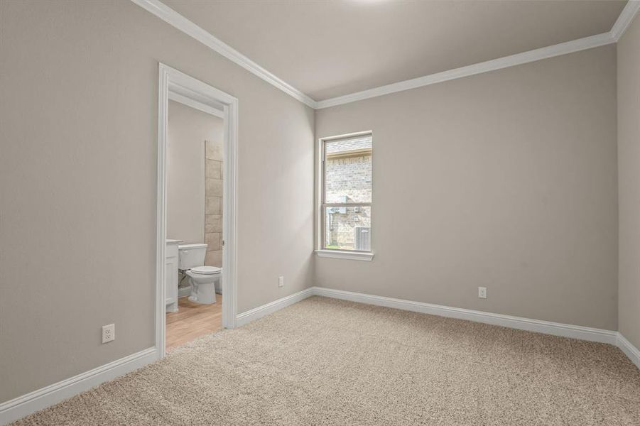 Unfurnished bedroom featuring light colored carpet, ornamental molding, and connected bathroom