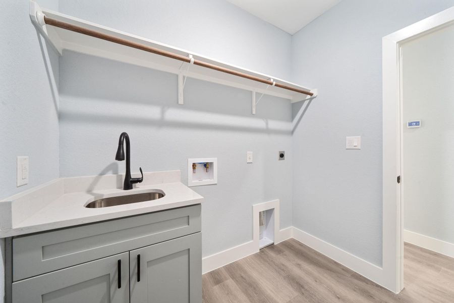 Utility room featuring a built-in sink with a matte black faucet, light grey cabinetry with black hardware, a light-colored countertop, and wood-finish flooring