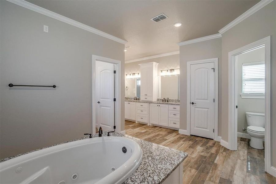 Bathroom with a bathtub, hardwood / wood-style flooring, toilet, vanity, and crown molding