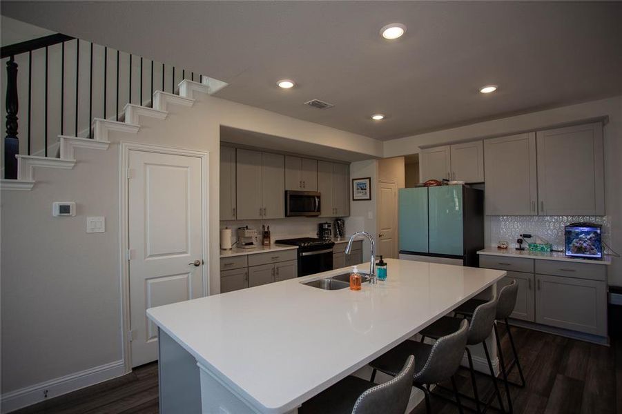 Kitchen featuring black gas range oven, stainless steel microwave, visible vents, freestanding refrigerator, and a sink