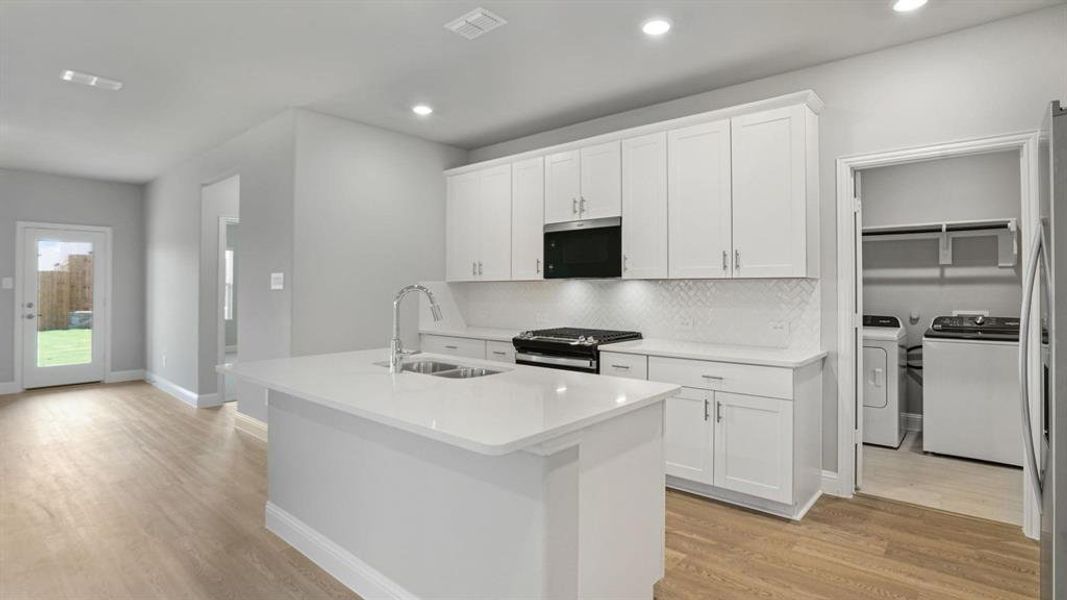 Kitchen with white cabinetry, stainless steel appliances, light wood-type flooring, decorative backsplash, and a center island with sink