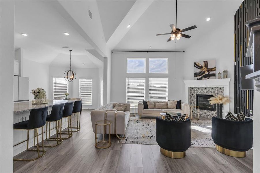 Living room with ceiling fan with notable chandelier, high vaulted ceiling, a tiled fireplace, and light hardwood / wood-style floors