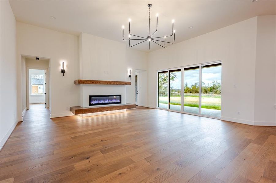 living room featuring light wood finished floors, a glass covered fireplace, healthy amount of natural light, and a chandelier