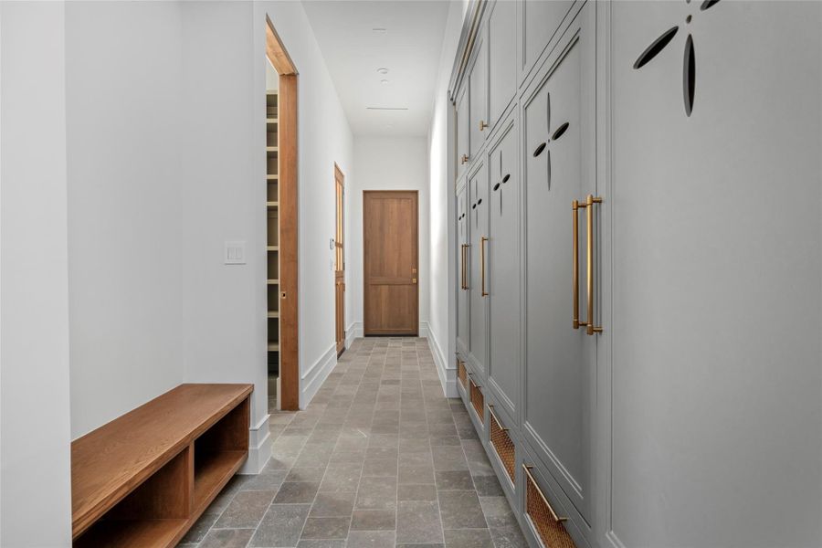 A thoughtfully designed transition to the laundry, mud room and home office pairs custom floor-to-ceiling cabinetry with warm brass accents and natural stone flooring. Generous concealed storage and a built-in bench keep everyday essentials beautifully organized while maintaining the home’s refined aesthetic. A thoughtfully designed transition to the laundry, mud room and home office pairs custom floor-to-ceiling cabinetry with warm brass accents and natural stone flooring. Generous concealed storage and a built-in bench keep everyday essentials beautifully organized while maintaining the home’s refined aesthetic.