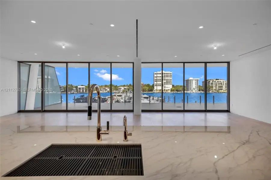 Countertop with an integrated drainboard and high-arc faucet, wood-finish flooring, and expansive floor-to-ceiling glass panels overlooking the waterfront