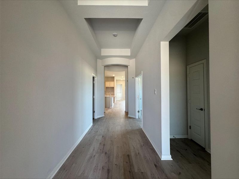 Corridor featuring wood finished floors, arched walkways, and a tray ceiling Corridor featuring wood finished floors, arched walkways, and a tray ceiling