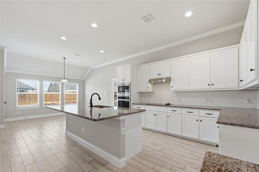Kitchen featuring dark stone counters, white cabinets, backsplash, vaulted ceiling, and crown molding Kitchen featuring dark stone counters, white cabinets, backsplash, vaulted ceiling, and crown molding
