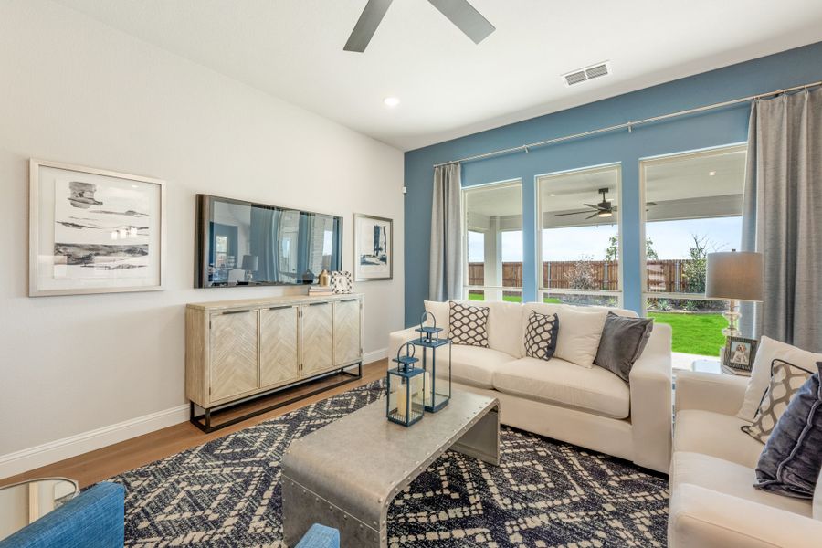 Living room with blue accent wall, white sofas, wall-mounted TV, and large windows overlooking backyard