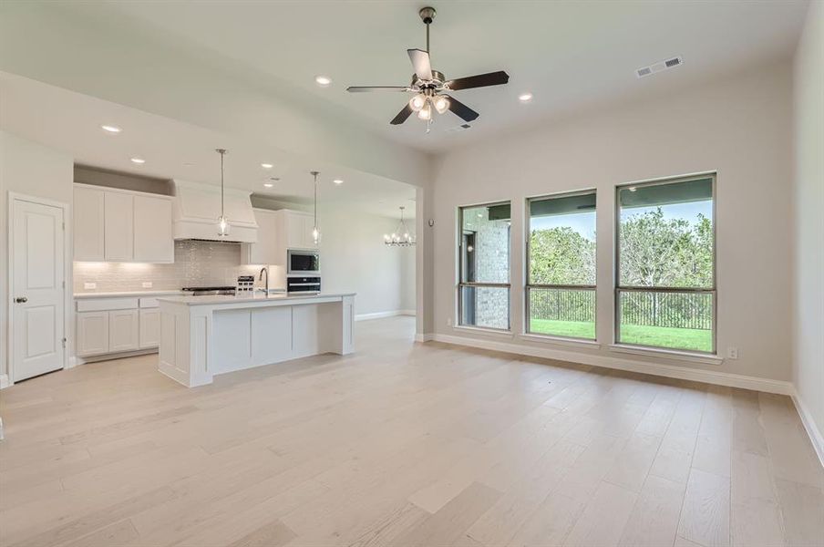 Kitchen with a center island with sink, backsplash, decorative light fixtures, oven, and white cabinetry