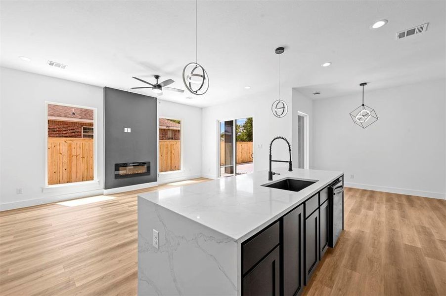 Kitchen with ceiling fan, light hardwood / wood-style flooring, pendant lighting, light stone countertops, and sink