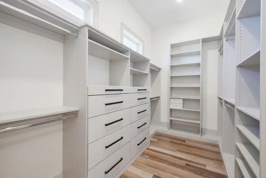 Expansive walk-in closet featuring built-in shelving, drawers with dark hardware, hanging rods, and wood flooring