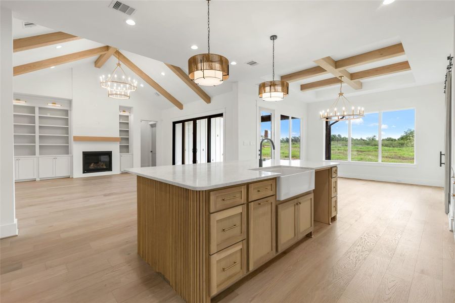 Kitchen with hanging lights, beam ceiling, open floor plan, light wood-style flooring, and a kitchen island with sink