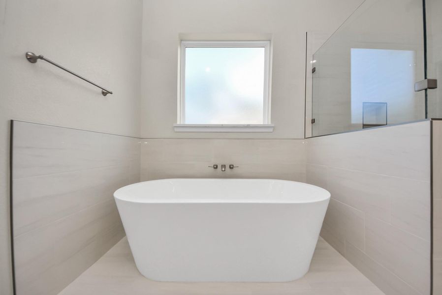 Also enjoy this freestanding white soaking bathtub, a frosted window for privacy, and sleek wall tiles in this primary bathroom retreat.